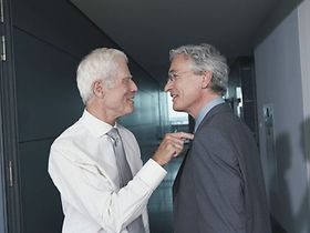 Mann tippt mit Finger auf Schulter von anderem Mann und lächelt