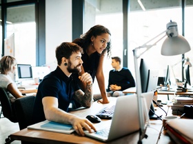 Two start up business people working together on a computer in modern office space