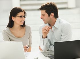 Mann und Frau sitzen an Laptops, unterhalten sich