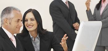 Mann und Frau vor Computer, Mann und Frau im Hintergrund