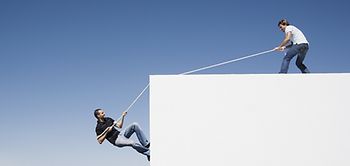 Mann zieht anderen Mann an Seil auf etwas hoch