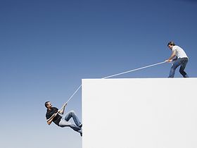 Mann zieht anderen Mann an Seil auf etwas hoch