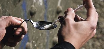 Mann zieht Spritze mit Heroin aus Loeffel auf, Detail