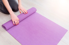 Young yoga Woman rolling her lilac mat after a yoga class on wooden floor near a window, close up