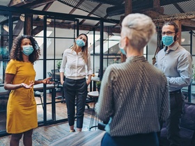 Group of entrepreneurs wearing masks and standing at a distance in the office
