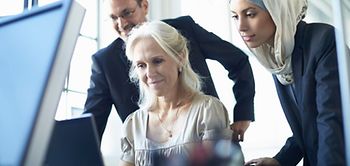 Mitarbeiterin mit Kopftuch schaut mit Kollegen auf Bildschirm