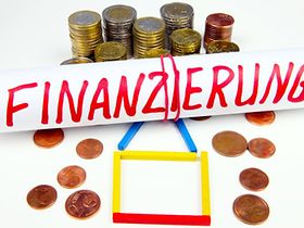Münzen und Haus aus Hölzern hinter Aufschrift Finanzierung