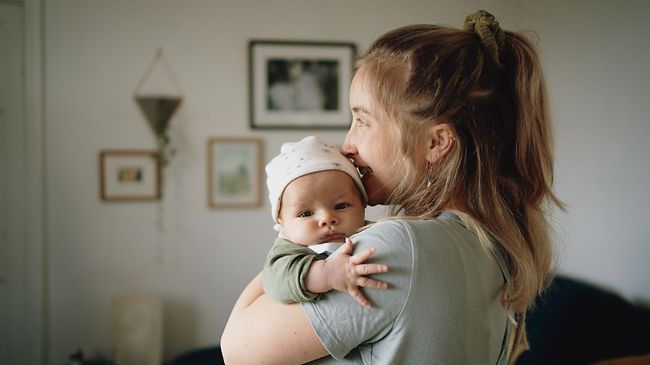 Mutter trägt Baby auf der Schulter welches aus dem Fenster schaut