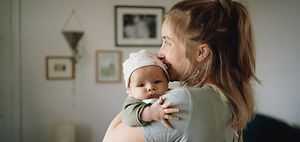 Mutter trägt Baby auf der Schulter welches aus dem Fenster schaut