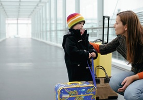 Mutter und Sohn stehen mit Koffern in einem Uebergang am Flughafen