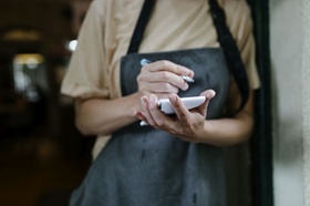 A waitress standing in the doorway of a restaurant and writing on her notepad.