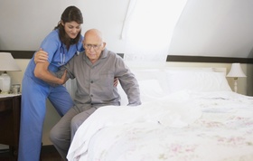 Pflegeperson die älterem Herr beim Aufstehen aus dem Bett hilft
