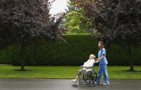 Pflegeperson die mit älterer Frau im Rollstuhl spazieren geht