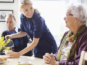 Pflegeperson schenkt altem Mann und alter Frau Kaffee ein