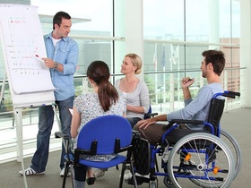 Präsentation an Flipchart vor Leuten von denen einer im Rollstuhl sitzt
