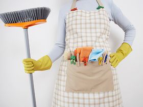 Putzfrau mit Schürze und Besen vor weißer Wand