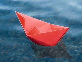 Rotes Papierschiffchen schwimmt auf Wasser