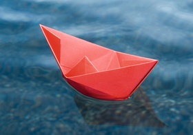 Rotes Papierschiffchen schwimmt auf Wasser