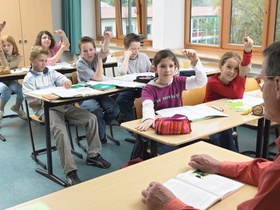 Schueler und Lehrer in Klassenzimmer, einige melden sich