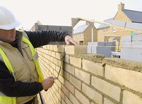 Schutzhelm und Warnweste tragender Mann baut Mauer
