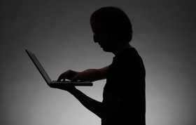 Silhouette einer Person die am Laptop arbeitet, Symbol: data theft, cyber crime