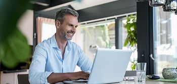 Smiling mature man at home using a laptop at table