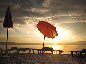 Sonnenschirm und Liegestuehle an Strand bei Sonnenuntergang