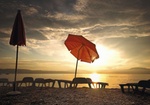 Sonnenschirm und Liegestuehle an Strand bei Sonnenuntergang