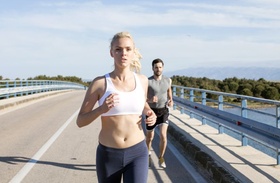 sportliches Paar joggt auf Brücke über Gewässer