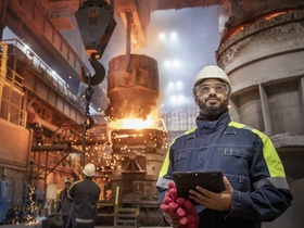 Stahlarbeiter mit Tablet in der Hand vor Hochofen