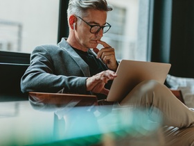 Businessman looking at laptop and thinking. Businessman reading emails on laptop in office lobby.