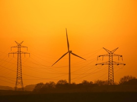 High-voltage electricity pylons - transmission towers and wind turbine silhouetted against sunset. (
