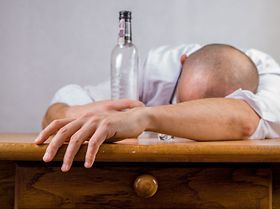 Sucht: Mann liegt mit Schnapsflasche auf dem Tisch