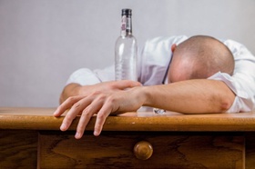 Sucht: Mann liegt mit Schnapsflasche auf dem Tisch