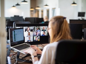 Businesswoman working on her laptop and having a video conference at her work desk. Rear view of a w