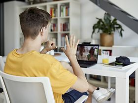 Over the shoulder view of relaxed teenage boy sitting at dining table and signing with his parents.