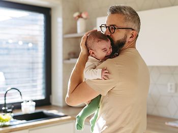 weinendes Baby in dem Arm vom Vater