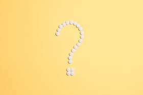 Weißes Fragezeichen aus Tabletten auf gelbem Grund