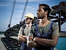 Zwei Arbeiter stehen in Kieswerk vor Stahlkonstruktion, Foerderband