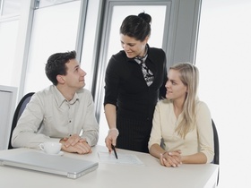 Zwei Frauen und ein Mann im Büro an Schreibtisch, Besprechung