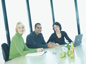 Zwei Frauen und ein Mann sitzen in Buero an Schreibtisch