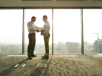 zwei Geschäftsmänner schütteln sich in hellem Büro die Hände