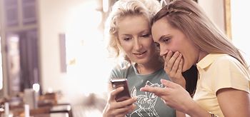 Zwei junge Frauen sehen sich in Cafe Foto auf Handy an