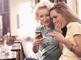Zwei junge Frauen sehen sich in Cafe Foto auf Handy an