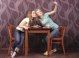 Zwei junge Frauen sitzen an Tisch und machen Selfie