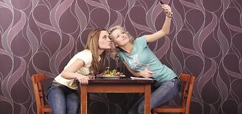 Zwei junge Frauen sitzen an Tisch und machen Selfie