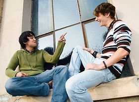 Zwei junge Maenner, einer asiatisch, sitzen aussen auf Fenstersim