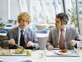 Zwei Männer sitzen in Kantine und unterhalten sich