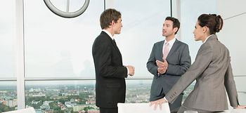 Zwei Maenner und Frau unterhalten sich stehend in Konferenzraum