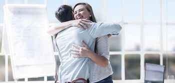 Zwei Mitarbeiter umarmen sich in hellem modernen Büro